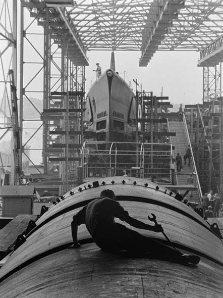 Photograph of a man working on the hull of a submarine at Electric Boat Co., Groton, Connecticut.